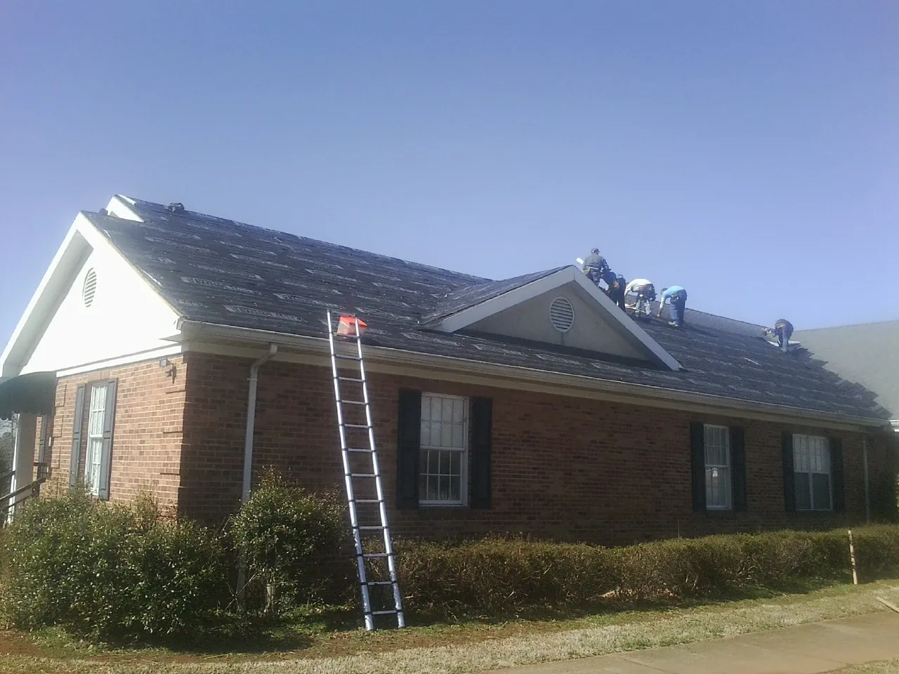 Crew tearing shingles off a brick ranch roof with a ladder set — Emergency Roof Repair work by our crew in Ottawa Lake