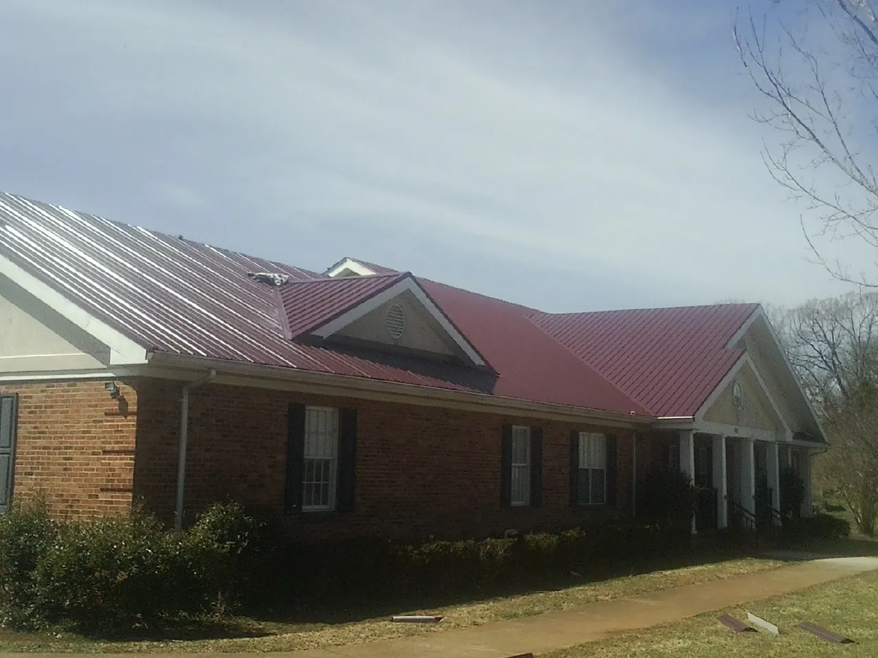 Red metal roof with gabled entries on a long brick building, from a Hail Damage Roof Repair job in Ottawa Lake