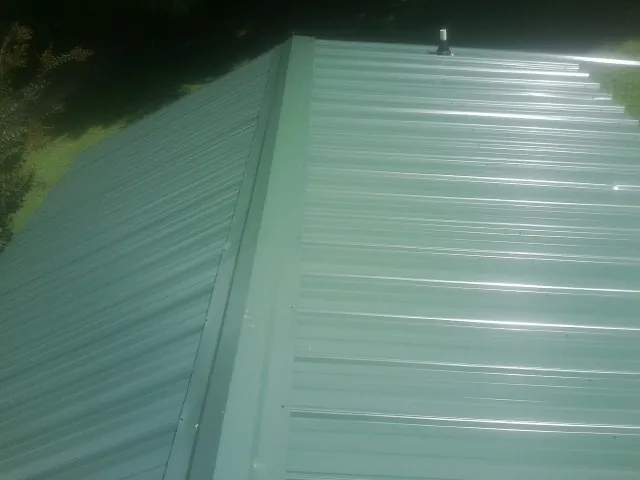 New green metal panels meeting at the ridge of a roof — Flat Roof Repair work by our crew in Ottawa Lake