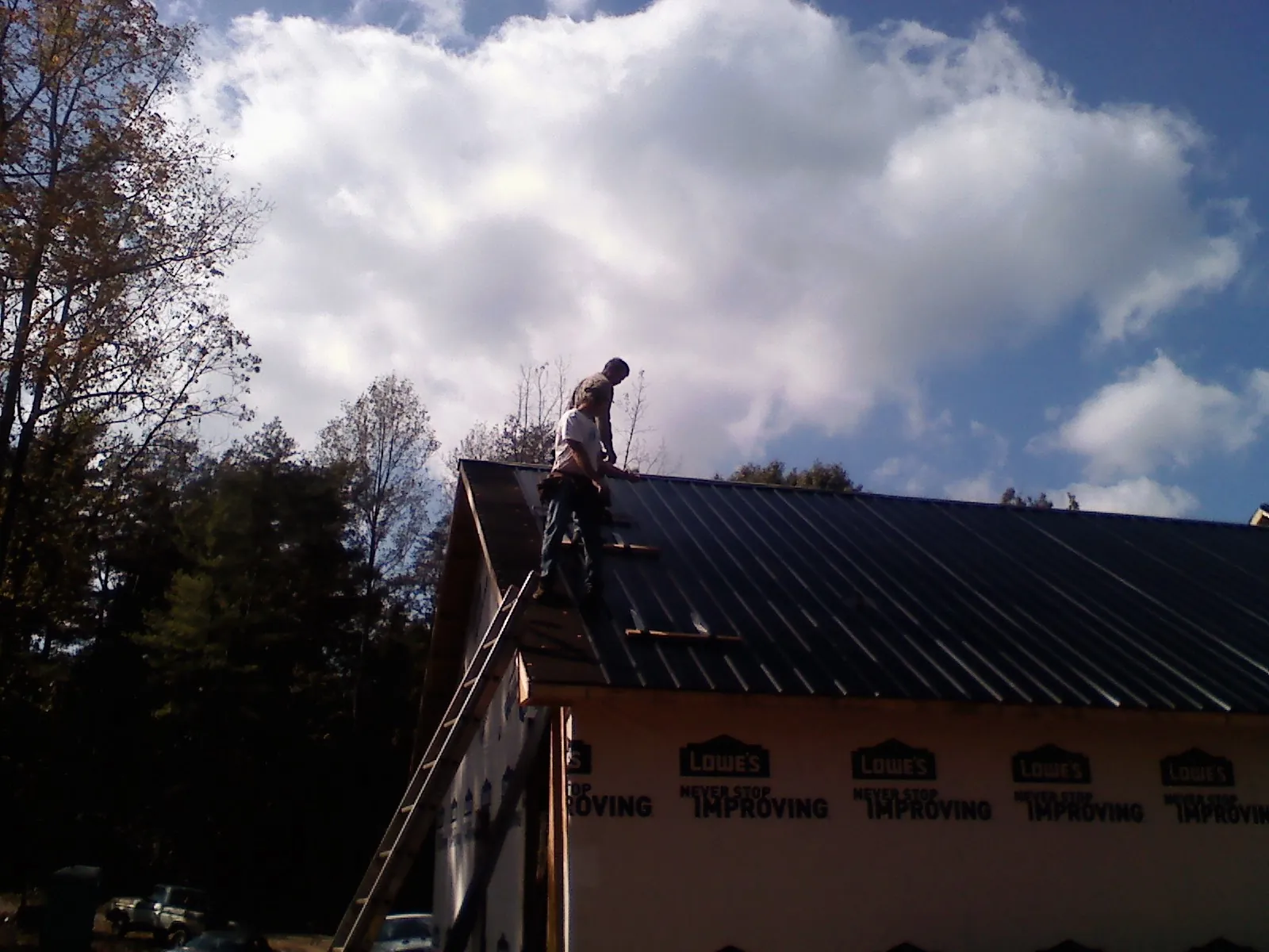 Roofer fastening dark metal panels high against a cloudy sky, from a Roof Inspection job in Ottawa Lake