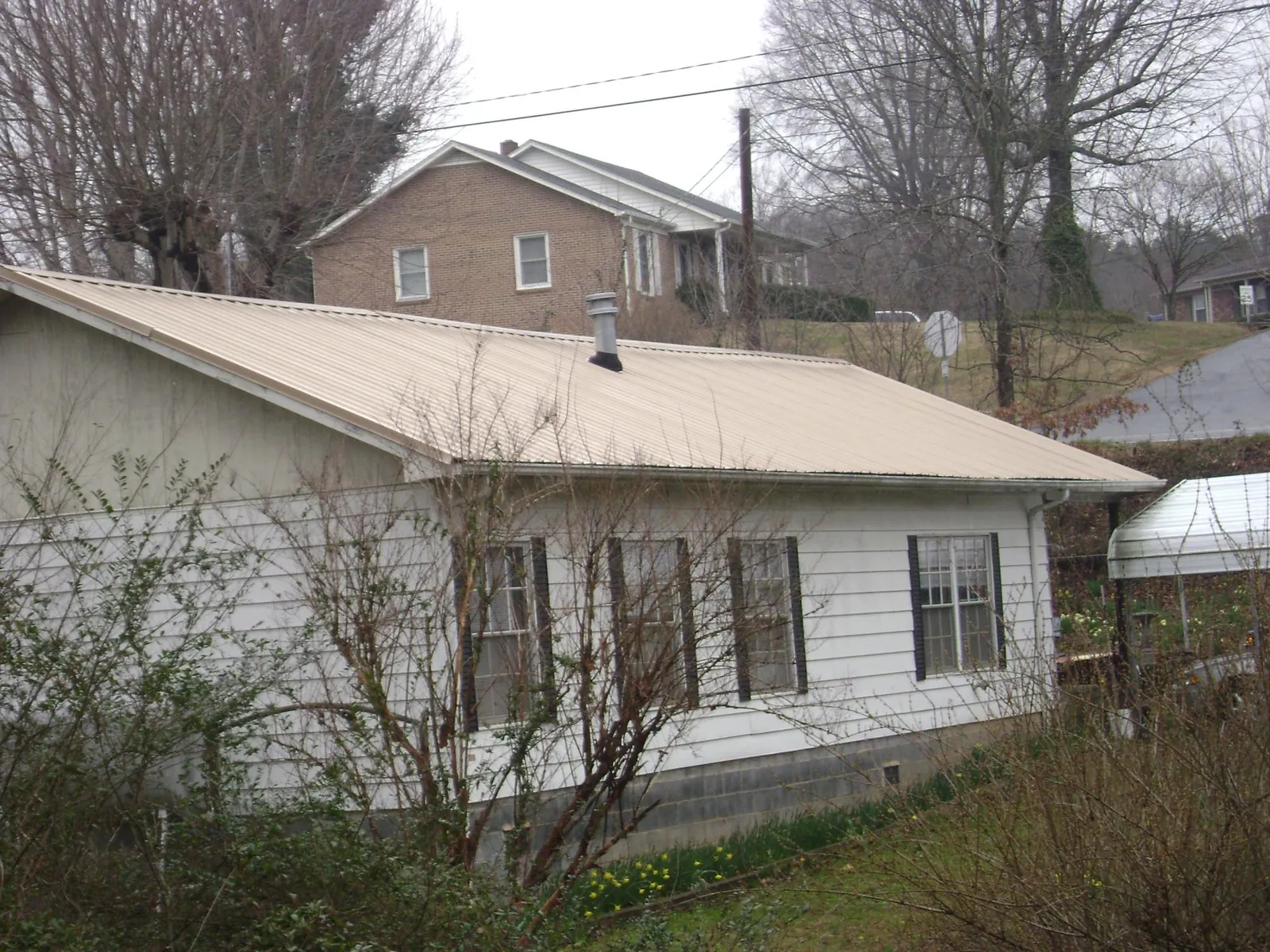 Tan metal roof on a white sided house set into a hillside — Commercial Roofing by Roofing Brothers in Ottawa Lake