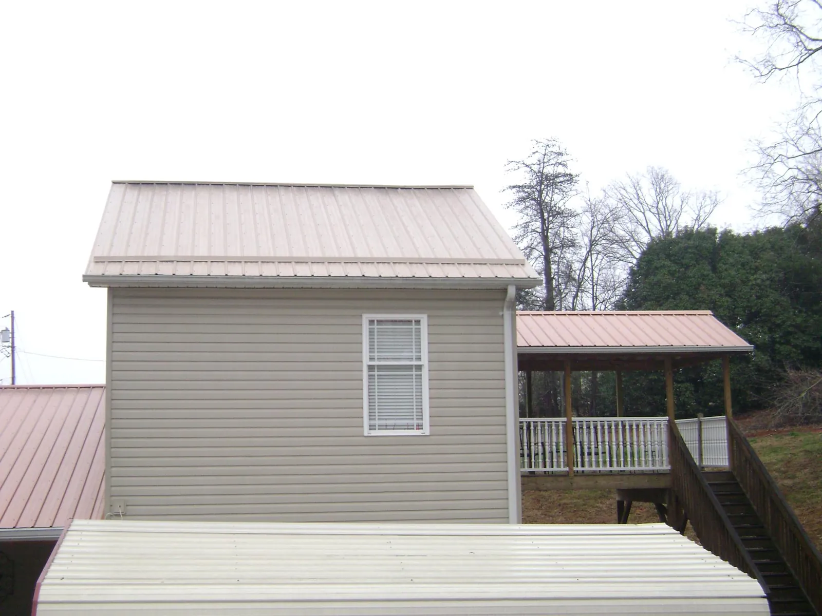 Tan metal roofs on a two story addition and attached porch, from a Roof Replacement job in Ottawa Lake